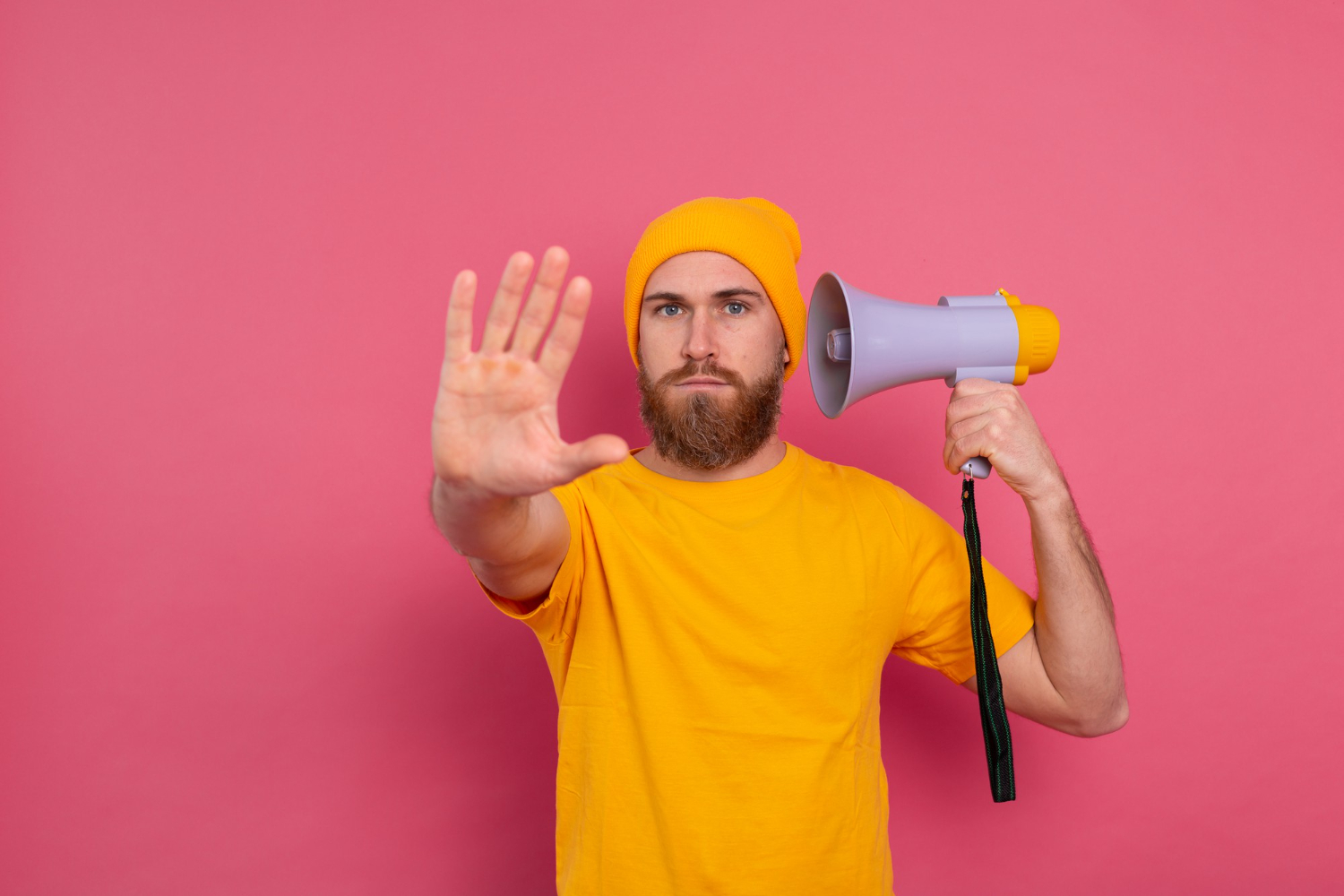 Un hombre barbudo vestido de amarillo sostiene un megáfono y levanta la mano sobre un fondo rosa, discutiendo apasionadamente sobre planes de pensiones.