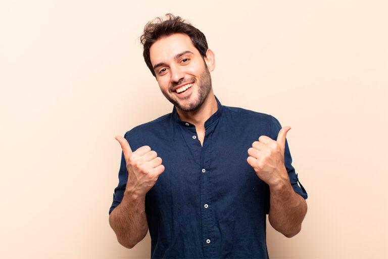 Un hombre sonriente con una camisa azul levanta los pulgares con ambas manos, simbolizando su satisfacción con sus cuentas nómina, todo ello sobre un fondo beige.