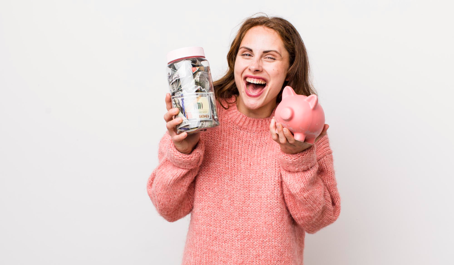 Una mujer con un suéter rosa sonríe cálidamente, sosteniendo un frasco de dinero junto a una alcancía rosa. Su confianza irradia mientras contempla las letras del tesoro, sabiendo que sus inversiones son inteligentes y seguras.