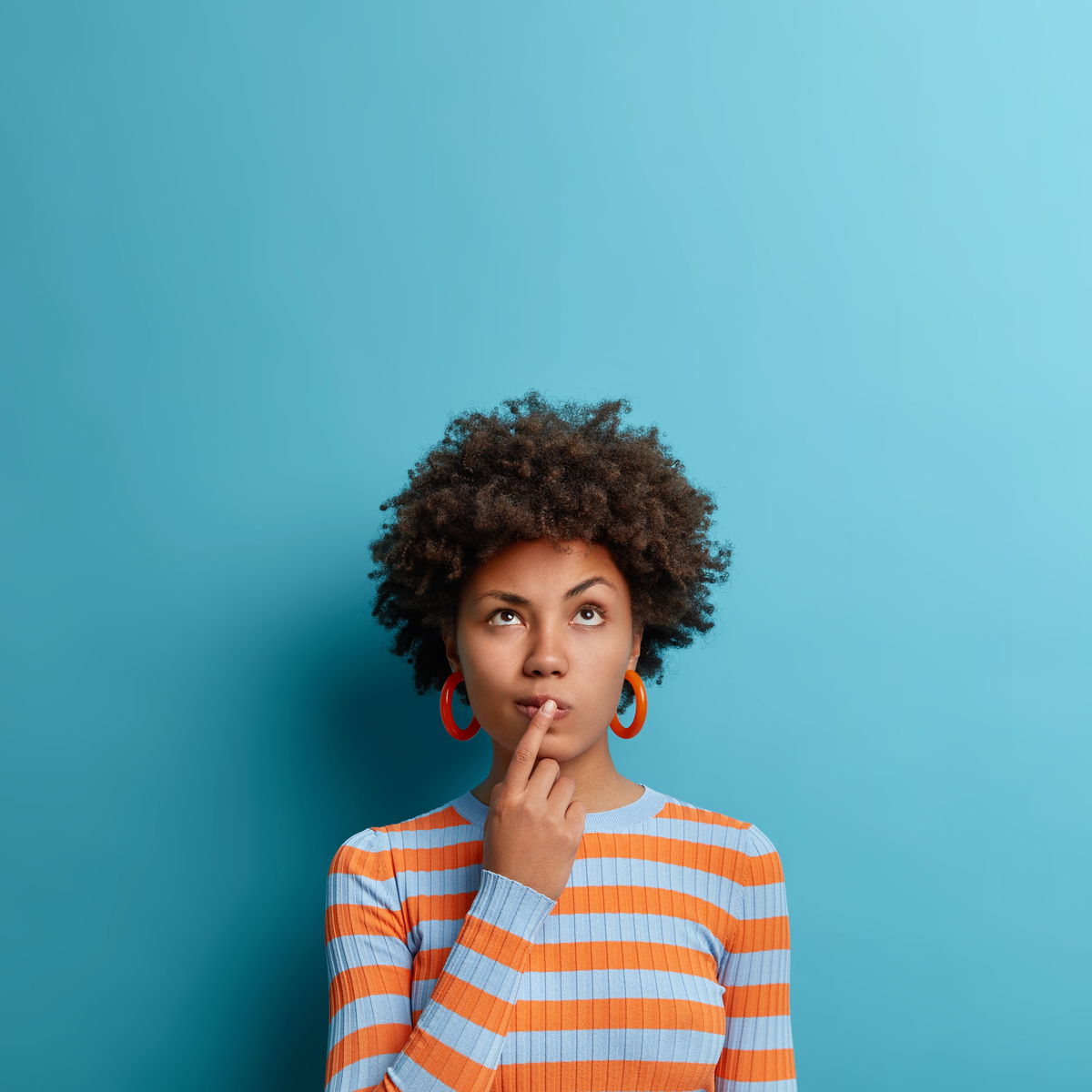 Una persona con cabello rizado, con un dedo en los labios, mira pensativamente hacia un fondo azul, como si contemplara los misterios que le aguardan y susurrara secretos del futuro.
