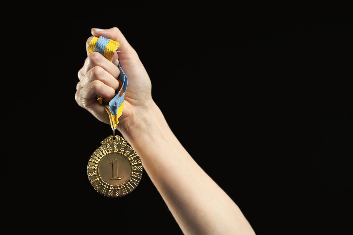 Una mano sostiene firmemente una medalla de oro con una cinta azul y amarilla, que brilla intensamente sobre un fondo negro, de forma muy similar a cómo un asesor robótico navega con precisión por las complejidades de los mercados financieros.