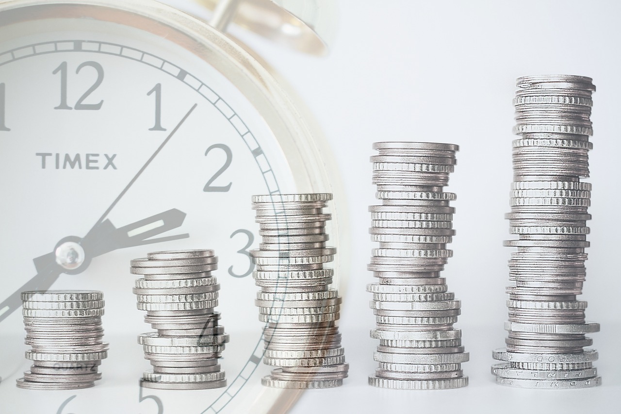 Pilas de monedas que aumentan de altura de izquierda a derecha están superpuestas a una esfera de reloj, que simboliza el valor del tiempo y el dinero en los planes de pensiones.