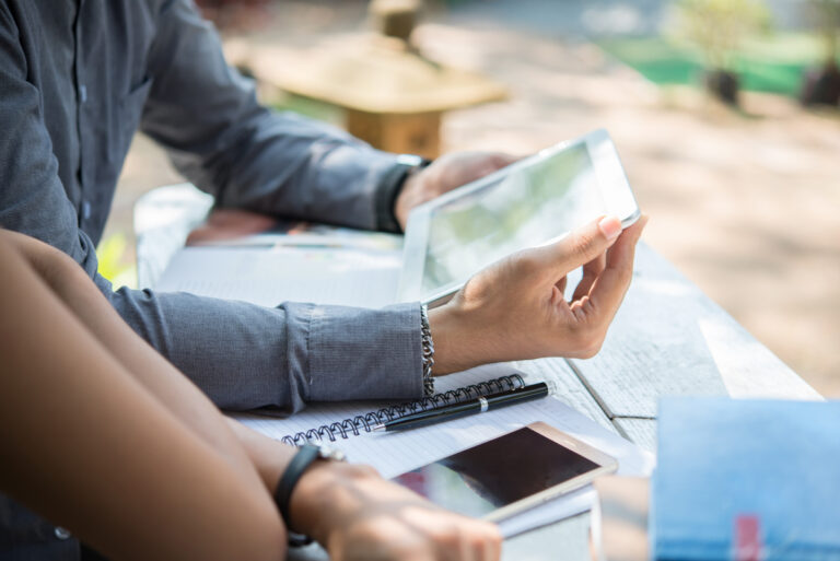 Dos personas en una mesa exploran la guía definitiva en una tableta y un teléfono inteligente, con cuadernos cerca, trazando sus próximos pasos.