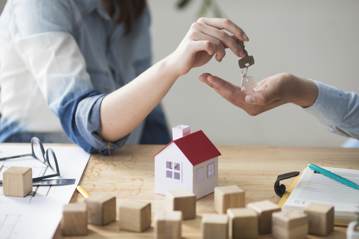 Una persona entrega las llaves de su casa sobre una mesa adornada con una pequeña maqueta de casa y bloques de madera, simbolizando el siguiente paso en su viaje con las hipotecas.