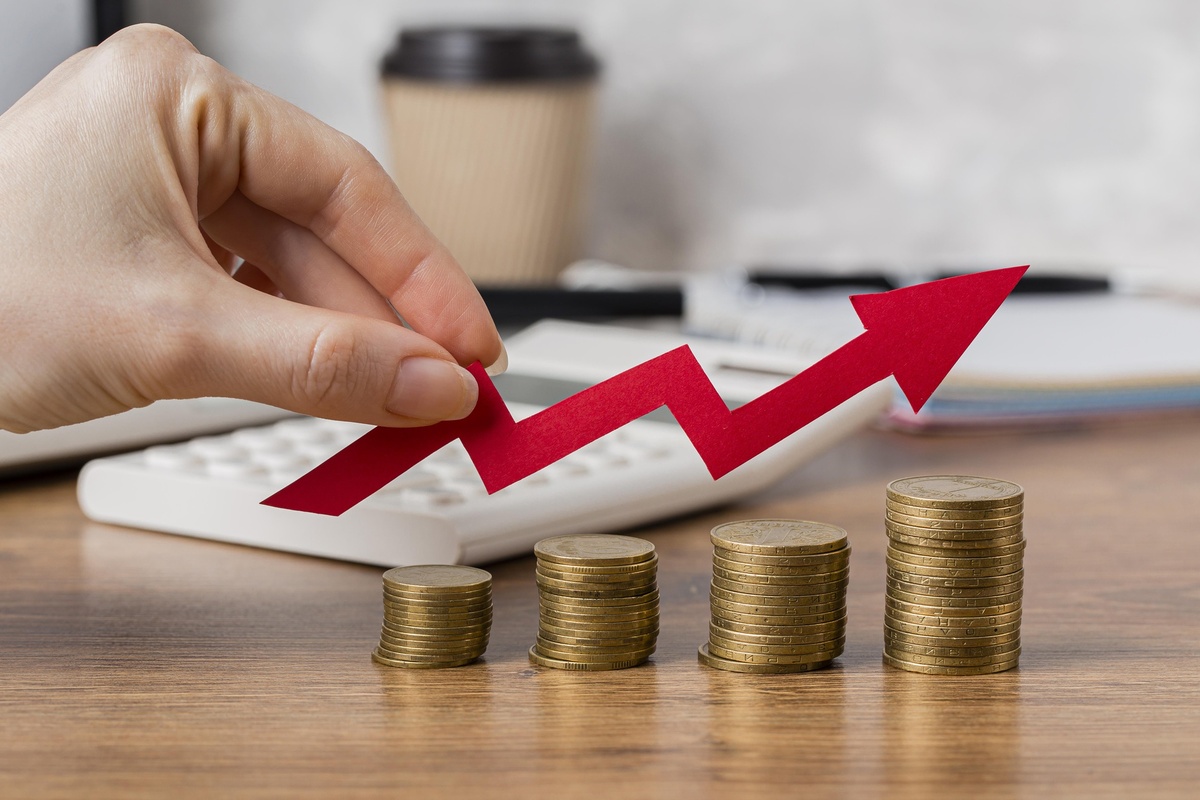 Una mano agarra una flecha roja hacia arriba sobre pilas de monedas, con una calculadora en el fondo, lo que simboliza el crecimiento financiero y la gestión eficaz de los fondos.