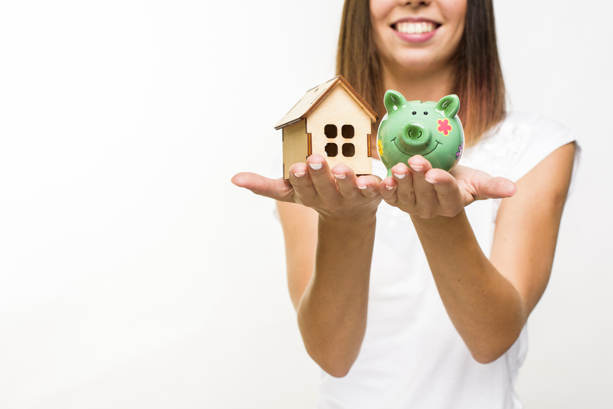 Mujer sonriente sosteniendo una pequeña casa de madera y una alcancía verde en sus manos, simbolizando el ahorro para una vivienda con una hipoteca de interés mixto.