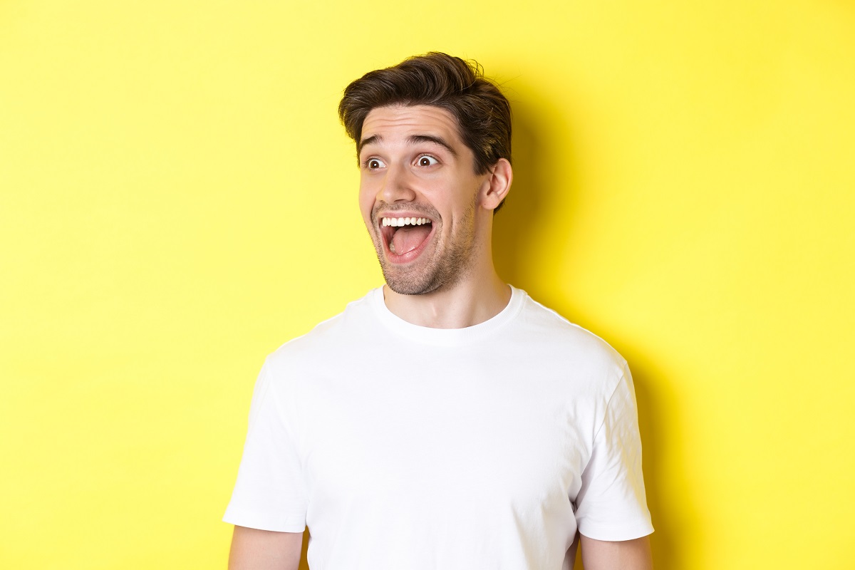 Hombre con camiseta blanca sonriendo ampliamente sobre fondo amarillo, como si celebrara con optimismo la última bajada del Euríbor pese a los rumores de recesión global.