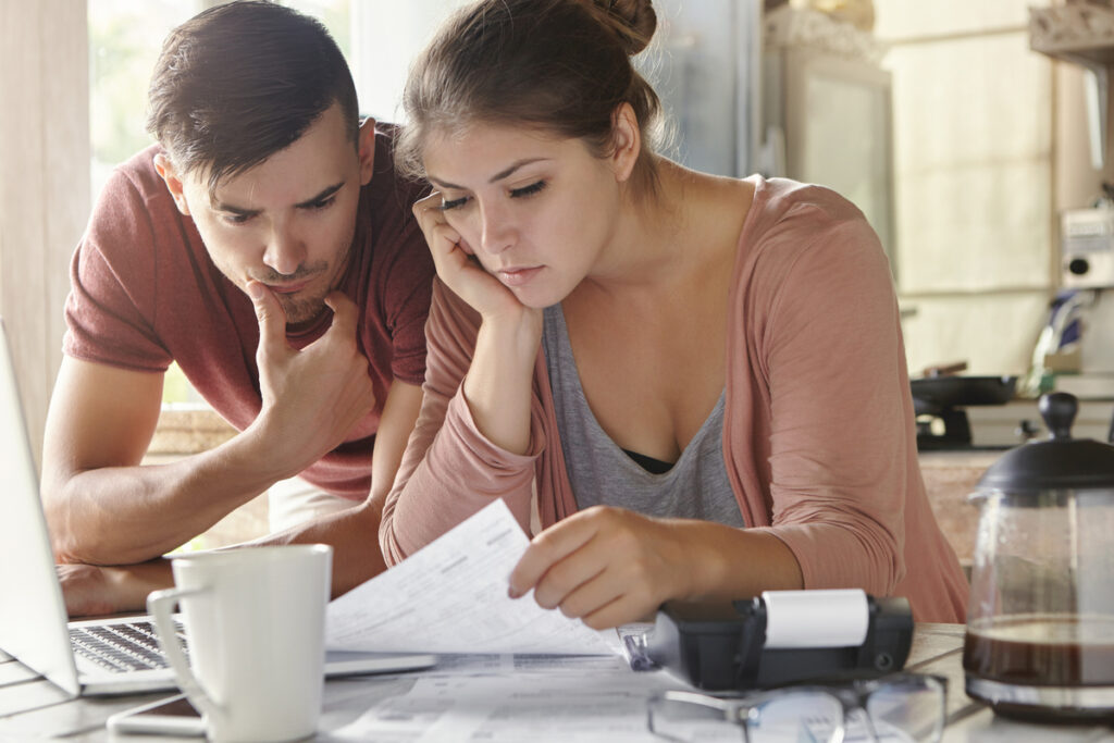 Una pareja revisa papeles en una mesa con una computadora portátil, café y una calculadora, administrando sus cuentas compartidas.