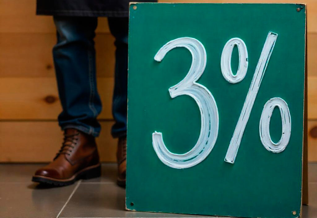 Un cartel verde con "3%" escrito en blanco, haciendo referencia a una cuenta remunerada; una persona con jeans y botas marrones está detrás.