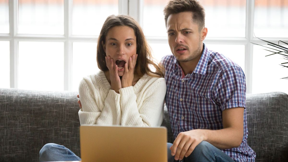 Una mujer sorprendida y un hombre preocupado se sientan en un sofá, mirando una pantalla de computadora portátil frente a ellos, preocupados por la inversión y el costo que implica vender con miedo.