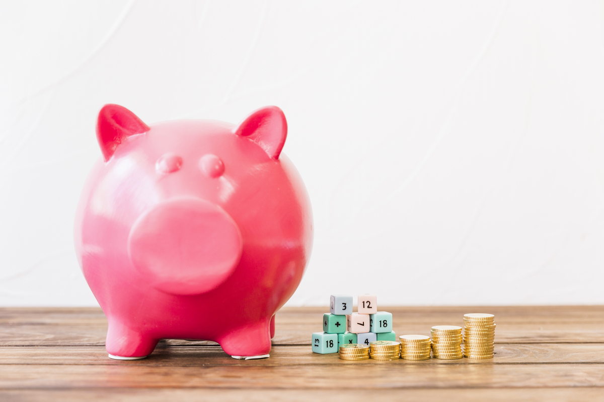 Una alcancía rosa junto a dados y montones de monedas de oro sobre una superficie de madera, que simboliza cómo elegir los mejores depósitos para tus ahorros.