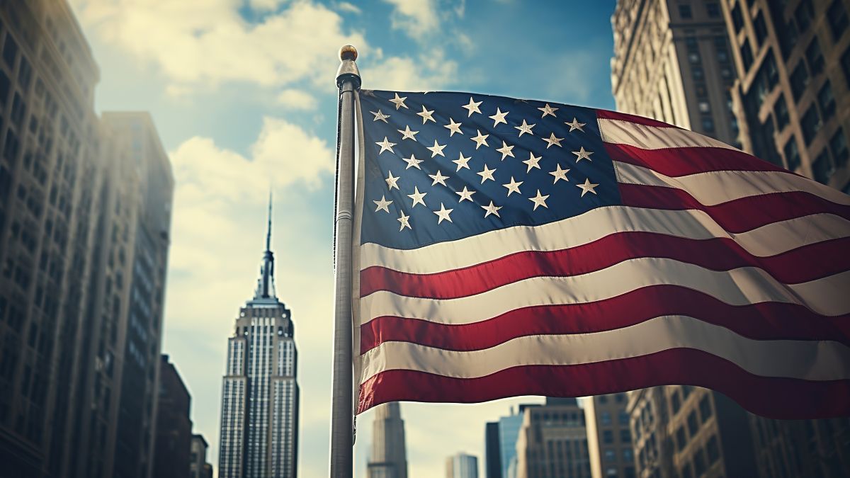Bandera estadounidense ondeando frente a altos edificios de la ciudad, con el Empire State Building al fondo.