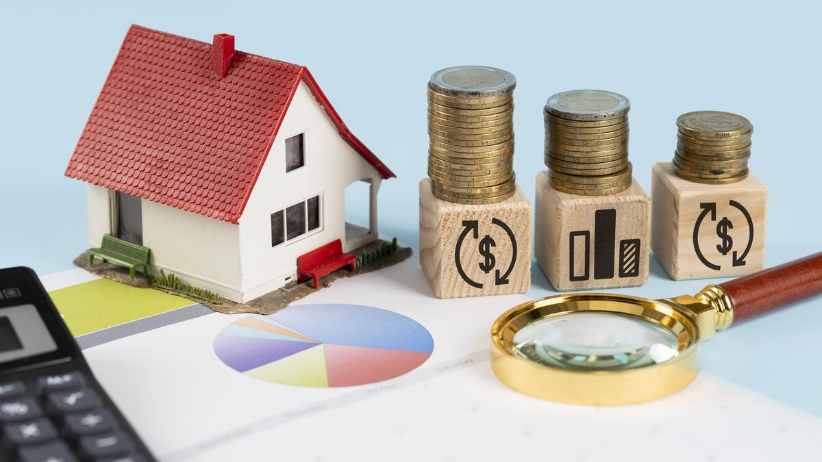 La casa modelo, las pilas de monedas sobre bloques, la lupa y los gráficos simbolizan la planificación financiera, la inversión y la gestión de los gastos hipotecarios.