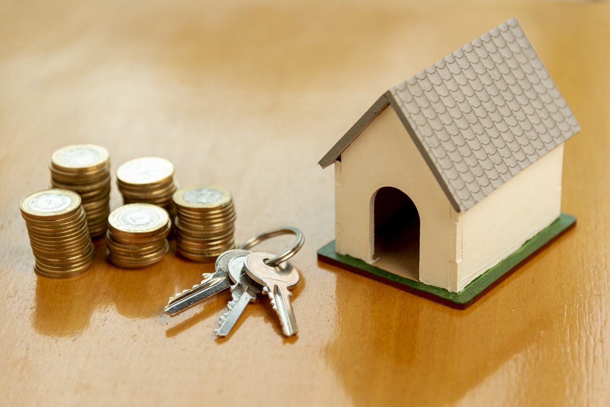 Tres pilas de monedas, dos llaves y una pequeña maqueta de casa sobre una superficie de madera, simbolizando las hipotecas de tipo fijo y el aumento récord de las hipotecas en euros en abril.