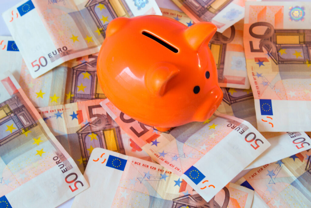 Una hucha naranja descansa sobre unos billetes de cincuenta euros esparcidos, lo que simboliza el potencial de ahorro que ofrecen las cuentas remuneradas.